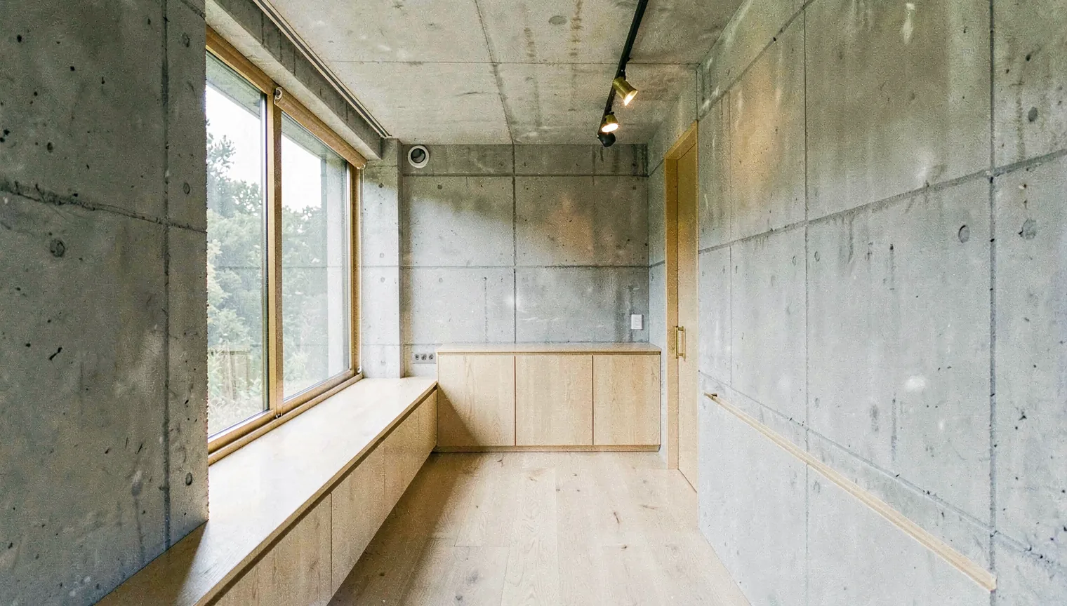 A daylit interior with concrete, oak, and a long window seat