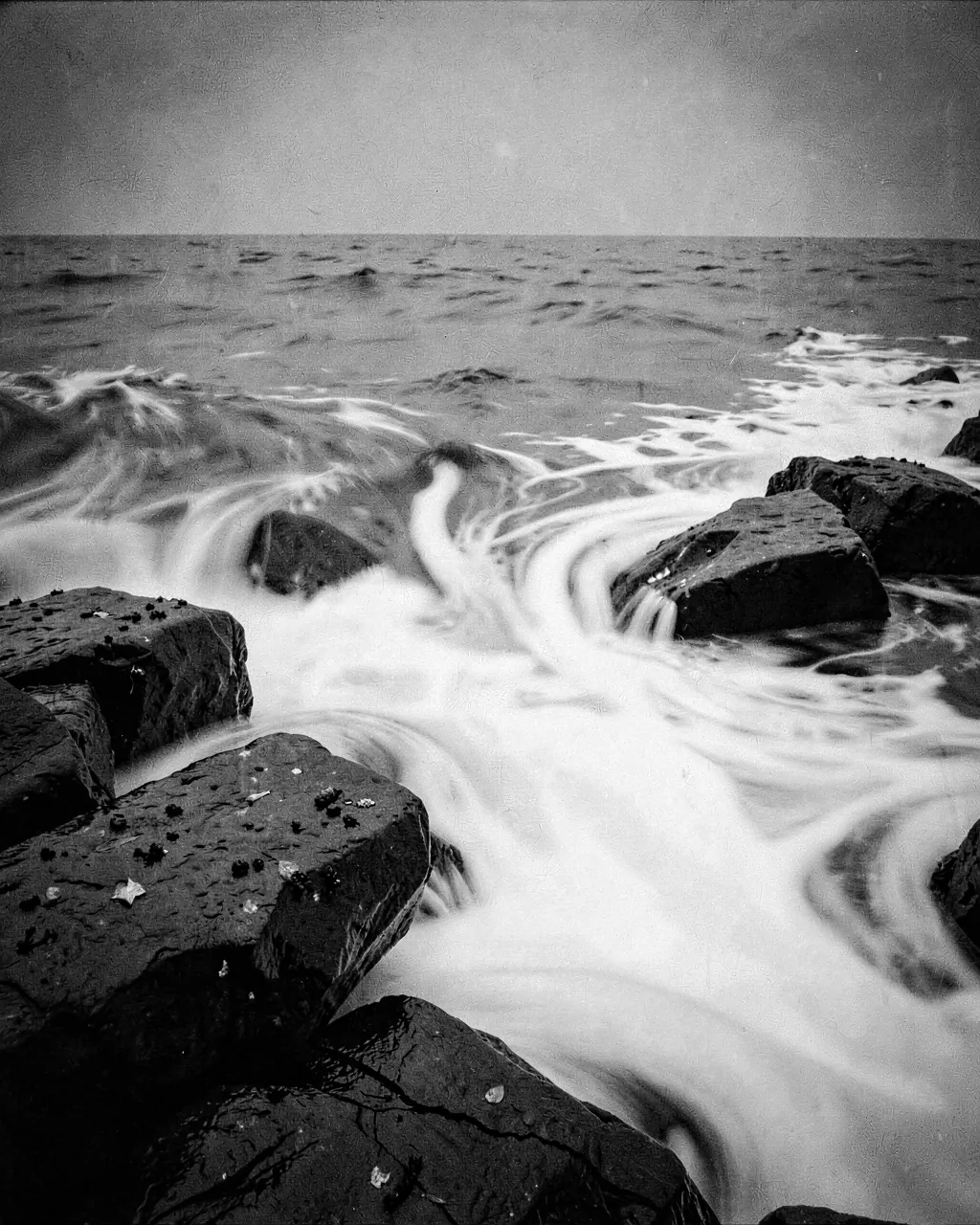 Long-exposure surf smoothed to silver around rocks