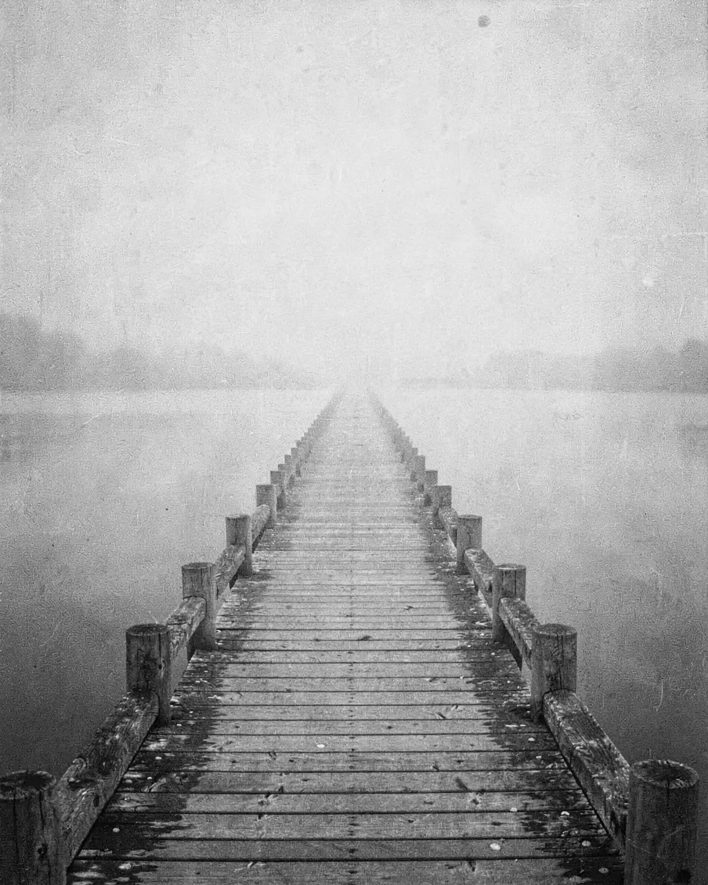 A pier vanishing into fog over still water