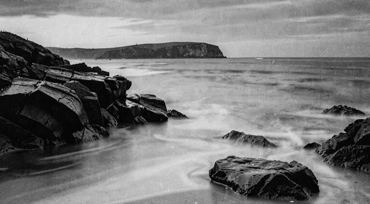 A long-exposure coastline at dusk, silver water against dark rock