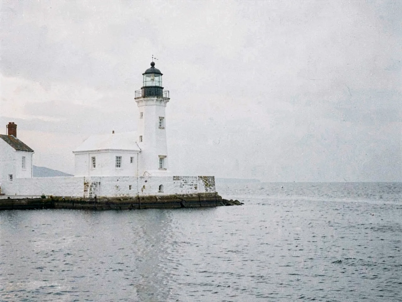 A whitewashed harbour light against a low grey sea at first watch