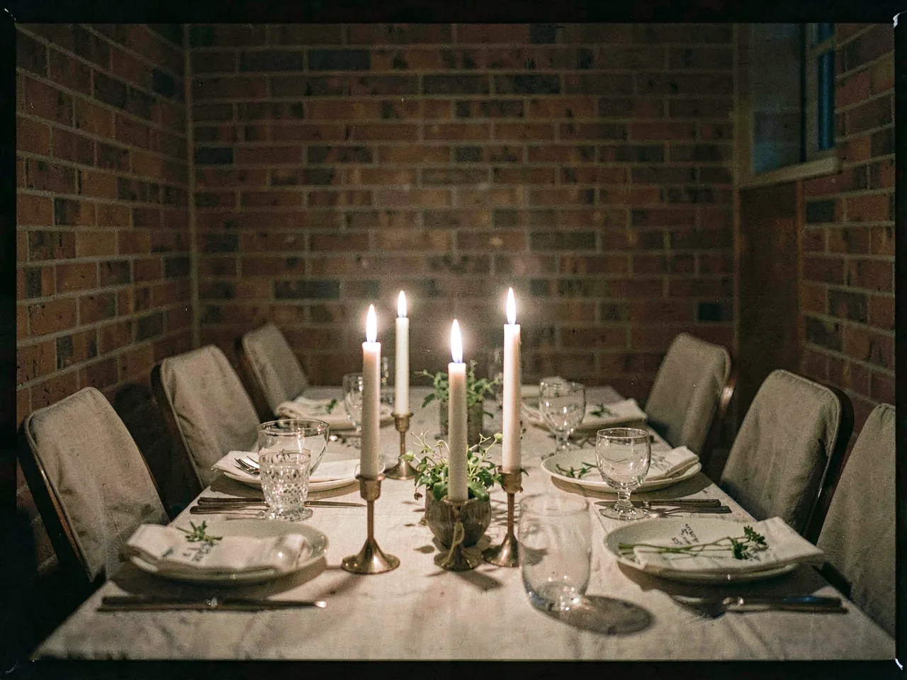 A long candlelit table laid for supper in a brick back room