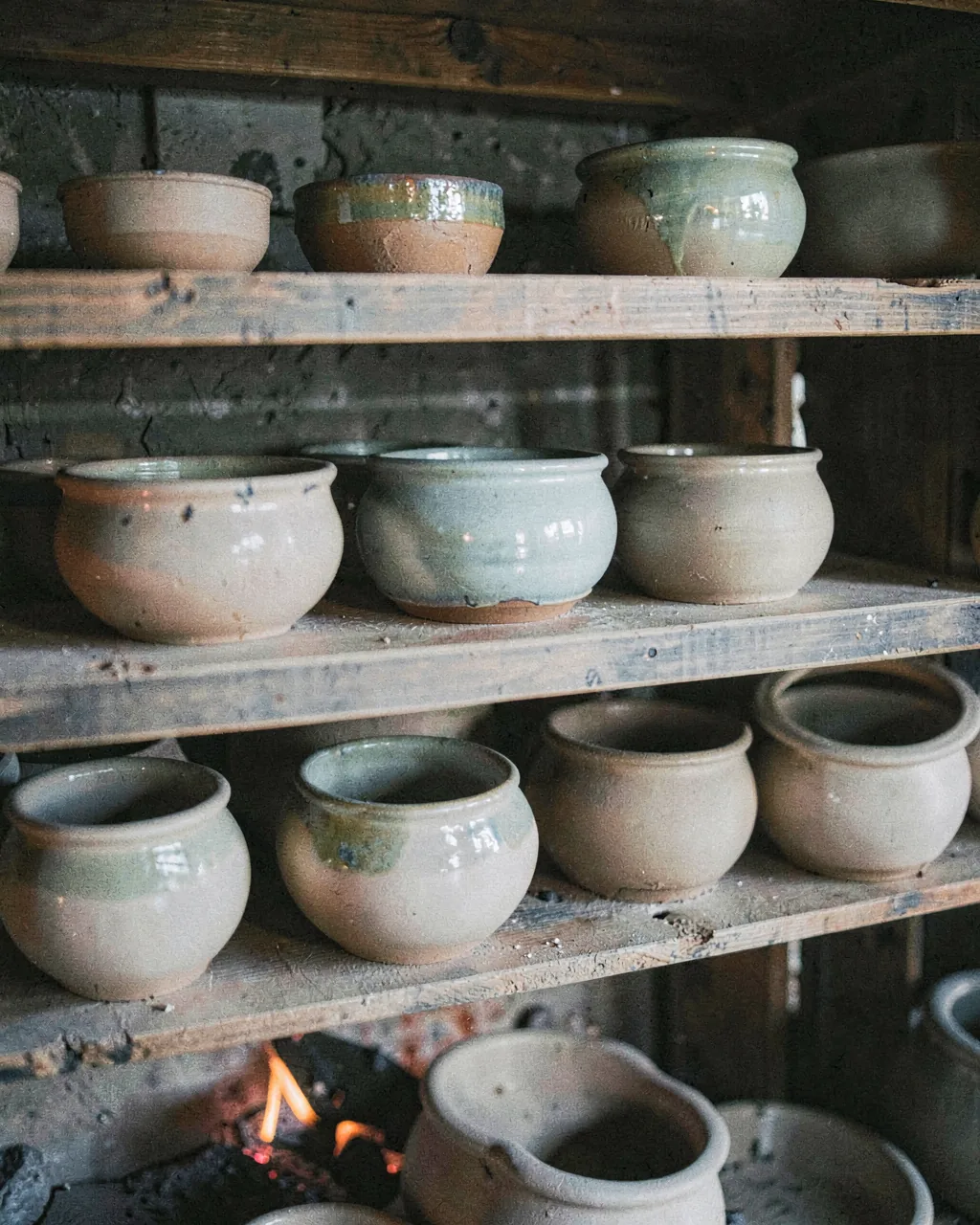 A loaded shelf inside a cooling wood-fired kiln, glaze still glassy
